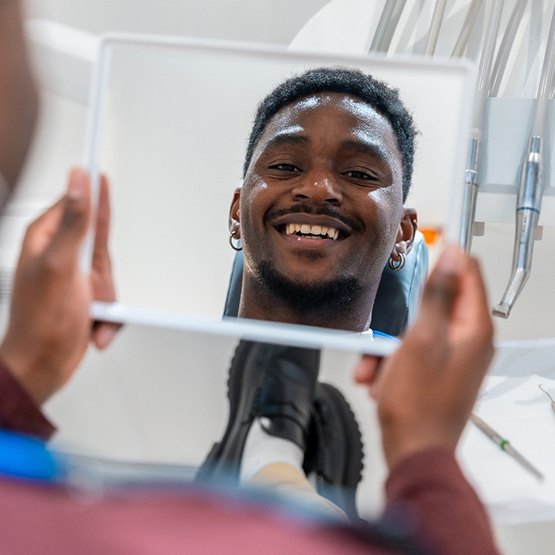 Male patient smiling in the mirror while in the dentist’s chair