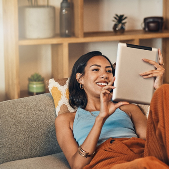 Smiling woman looking at tablet while relaxing on couch