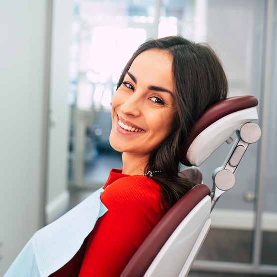 Woman in red shirt sitting in dental chair and smiling
